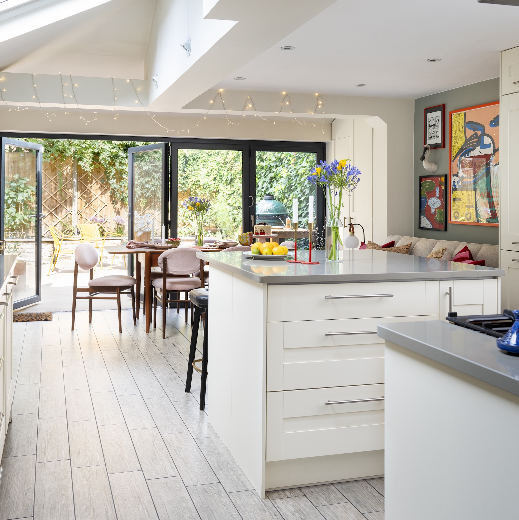 kitchen-diner in victorian extended house with patio doors to garden and dining table with pink velvet chairs, white island and white cabinetry