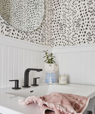A sink with black and white wallpaper, a pink towel, and black taps