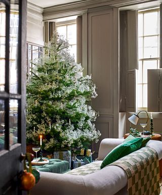 Living room with large christmas tree with flower and candle decorations, sofa, windows with shutters