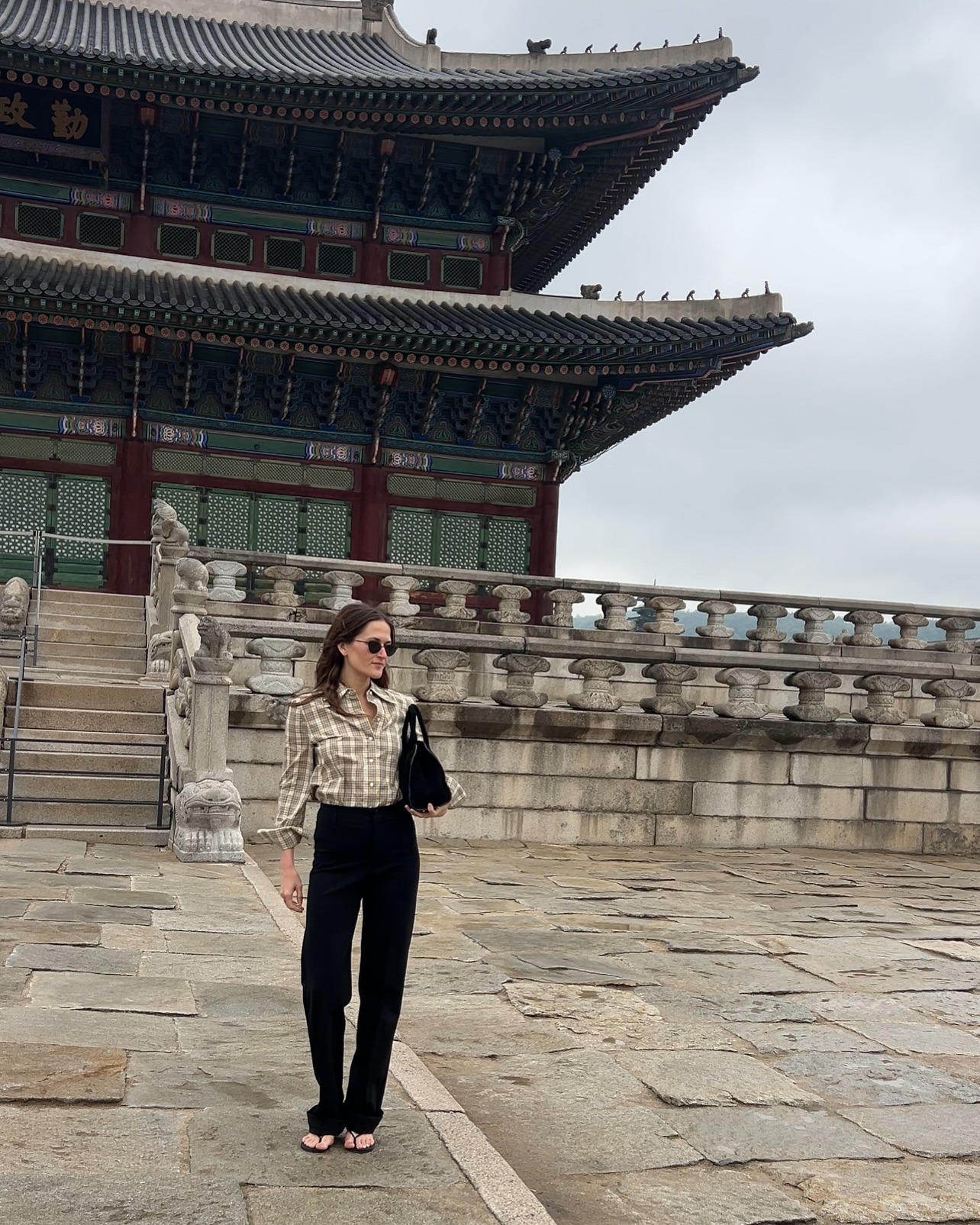 Eliza Huber in Seoul, South Korea wearing a plaid Tory Burch button-down shirt with black Kallmeyer pants and heeled flip flops from Studio Amelia.