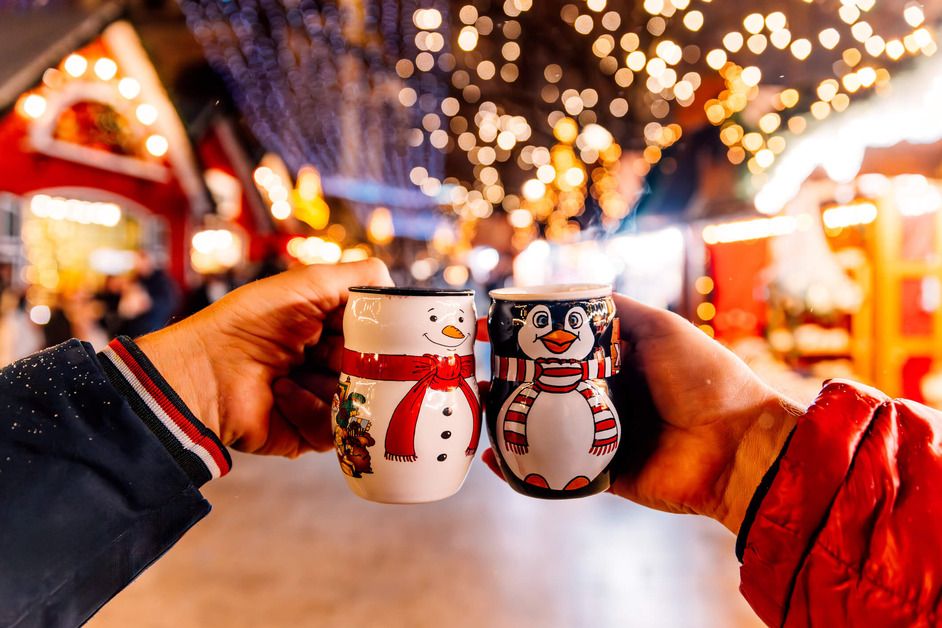Two Christmas mugs are held together with the Christmas market in the background.
