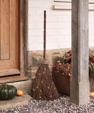 A porch with a brown broom, pumpkins and a basket on the stone gravel, above which stood a wooden beam