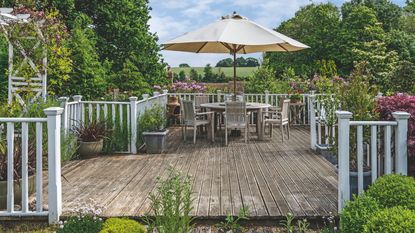 Large decking area surrounded by greenergy with table and chairs on it