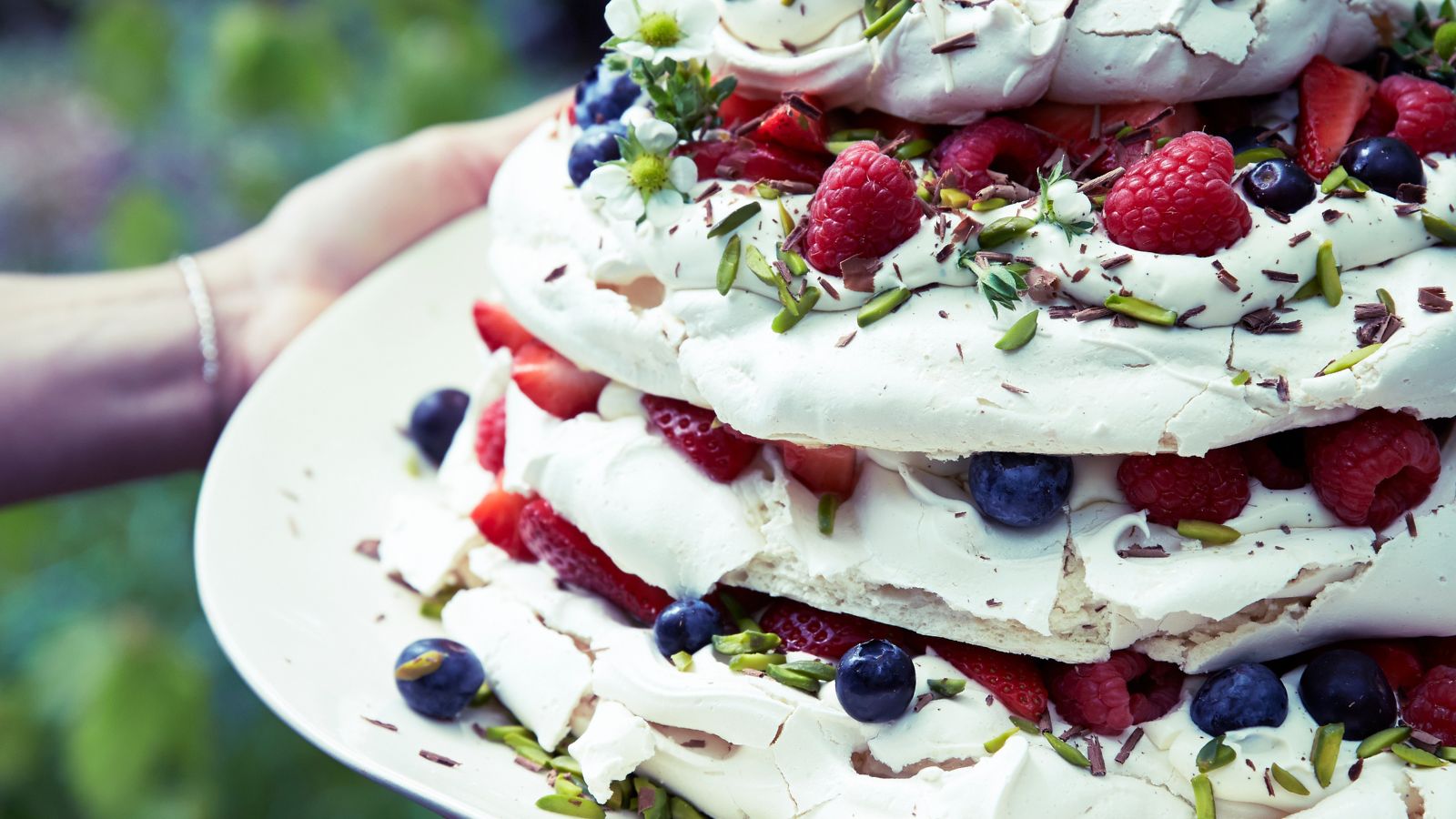 Meringue stack with summer berries on a plate with outdoor greenery in the background