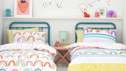 A kids bedroom with two beds with teal blue metal headboards and colourful rainbow bedding