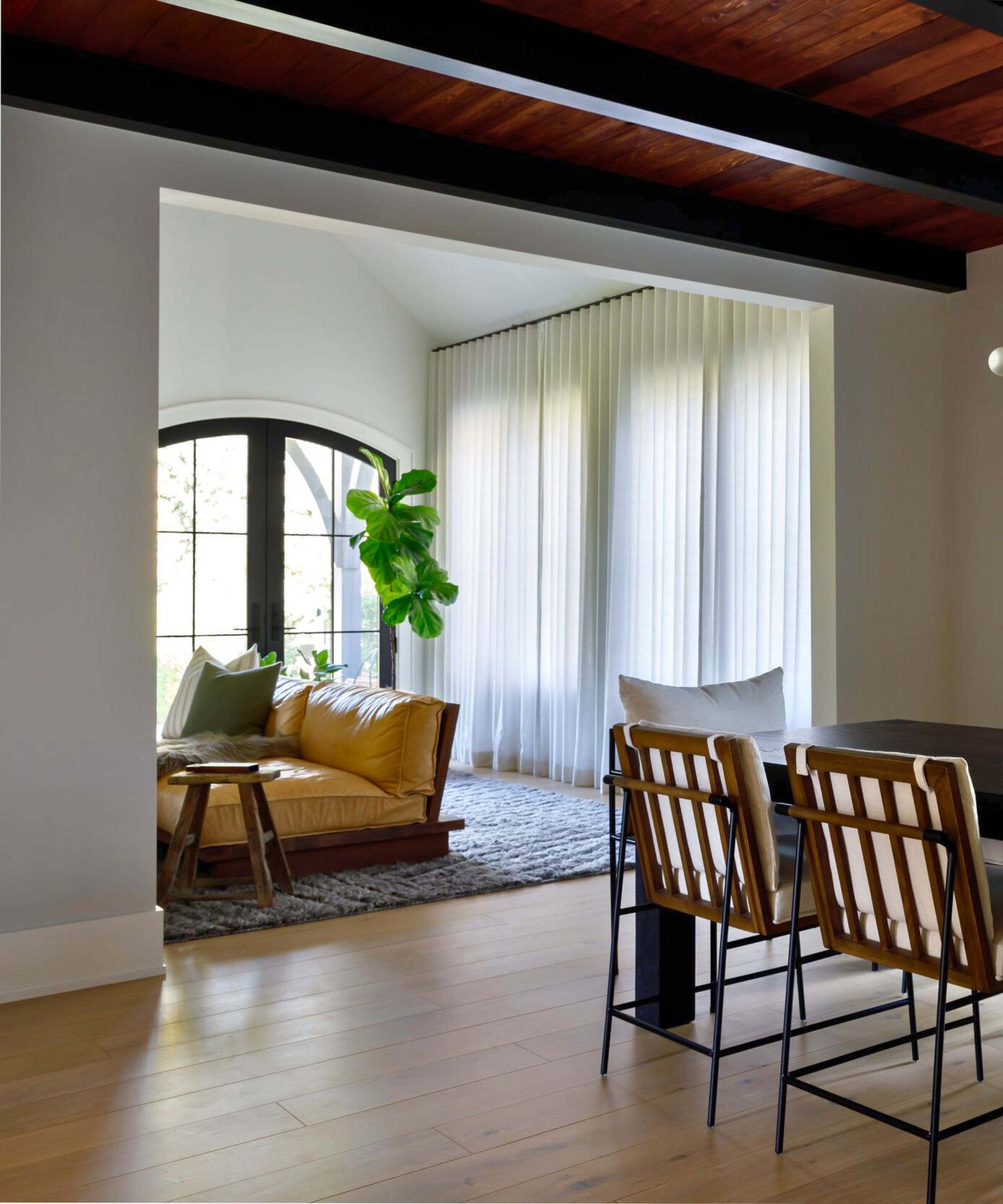 Semi-sheer net curtains in living room creating privacy for a large window. There is a butter yellow leather sectional in view, on a cozy blue-gray rug, and the corner of a chic dining table to the right in view