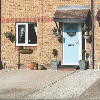 Concrete and gravel driveway in front of house with blue door