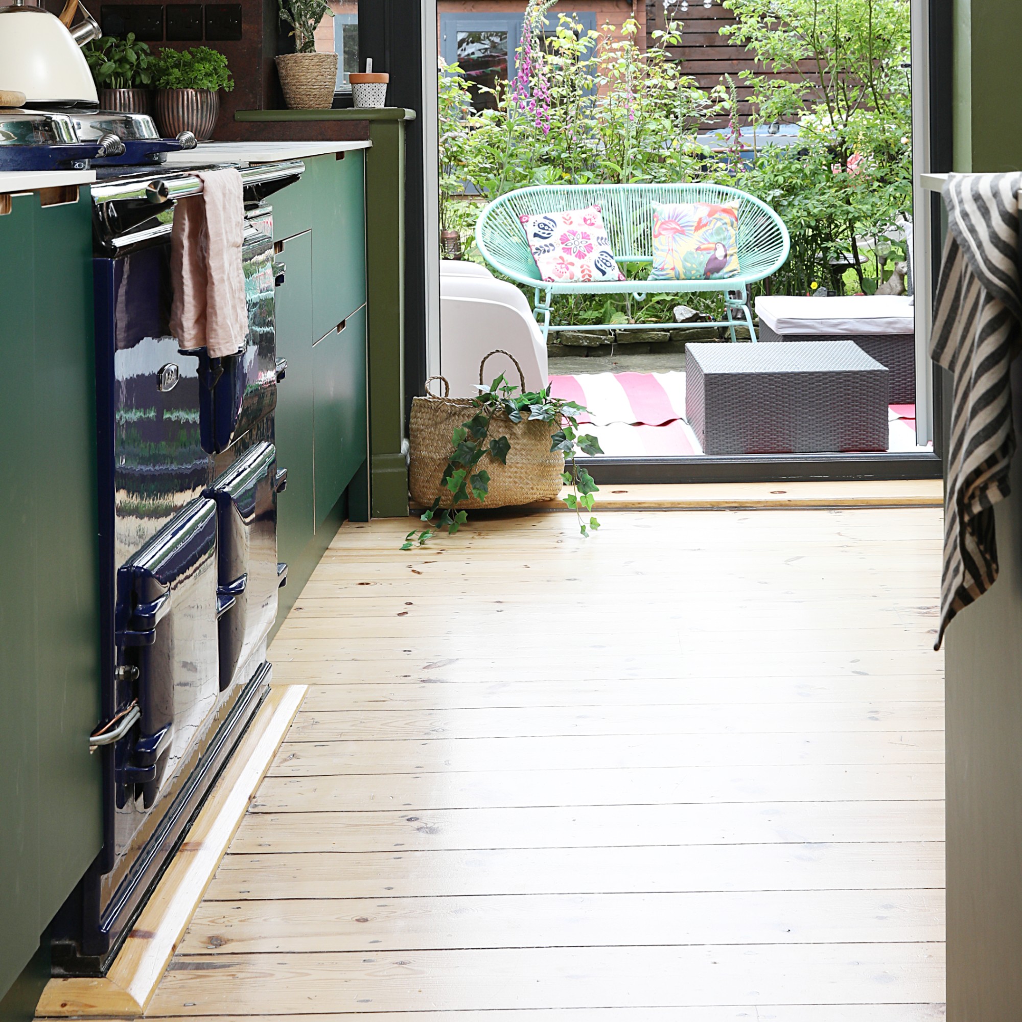 A green kitchen with open doors to a balcony with a green outdoor bench, a striped outdoor rug and a set of ottomans