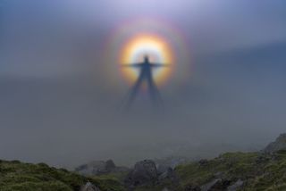 A photo showing the 'Brocken specter' -- an optical illusion that occurs when a figure's shadow looms enormous and glowing on a backdrop of cloud.