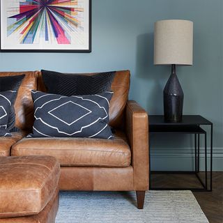 blue living room with tan leather sofa and black cushions and lamp