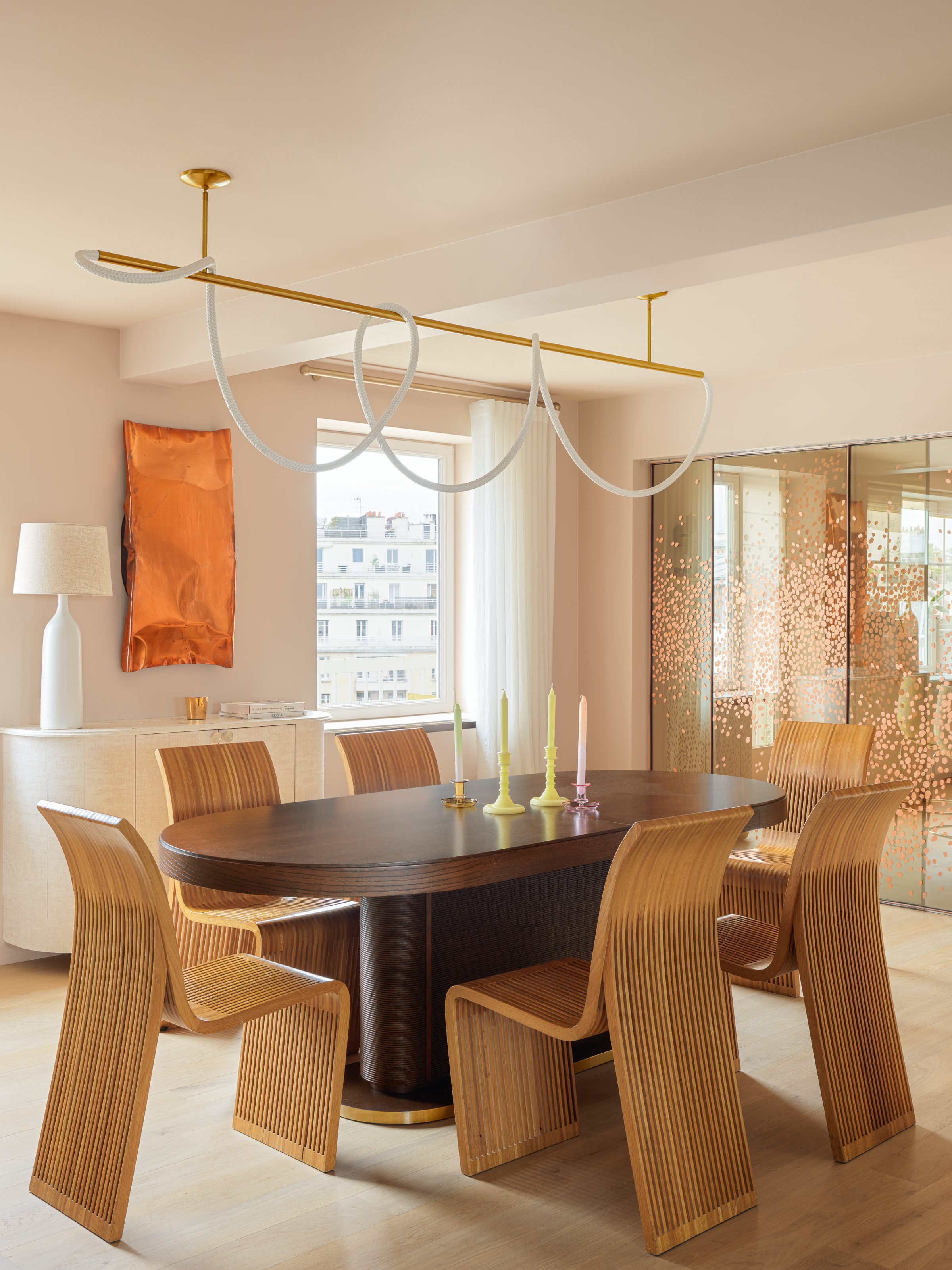 Dining room with slatted dining chairs and dark wood table, sculptural chandelier, orange metallic wall art and copper leaf panels