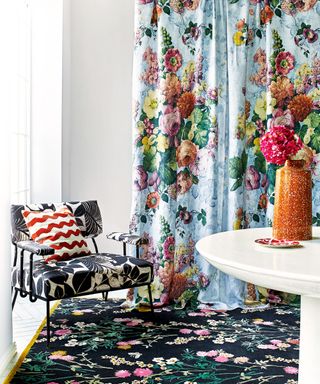 A blue floral drape with black patterned floral rug and armchair.