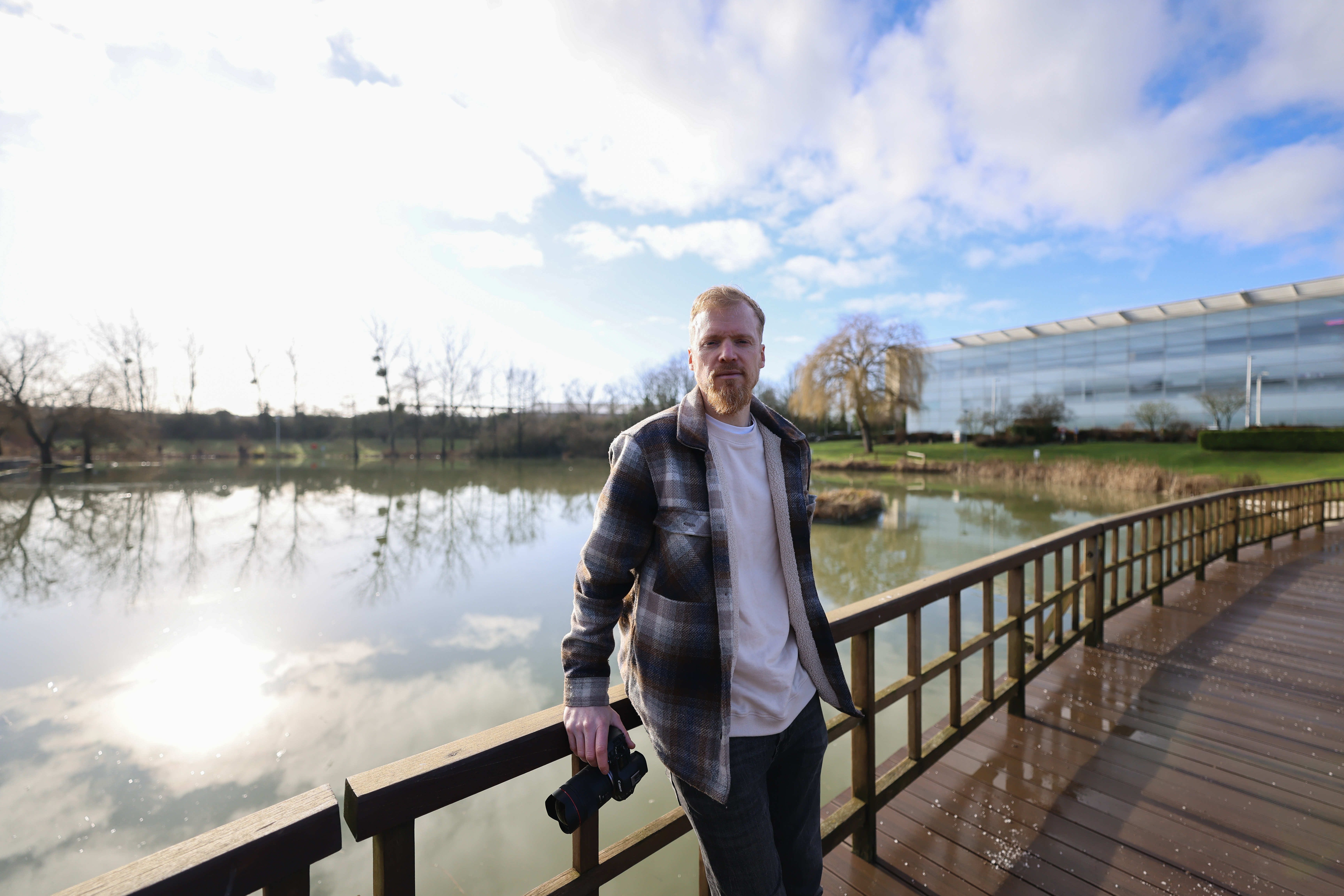 Techradar cameras editor Tim Coleman leaning on a wooden bridge in front of the lake