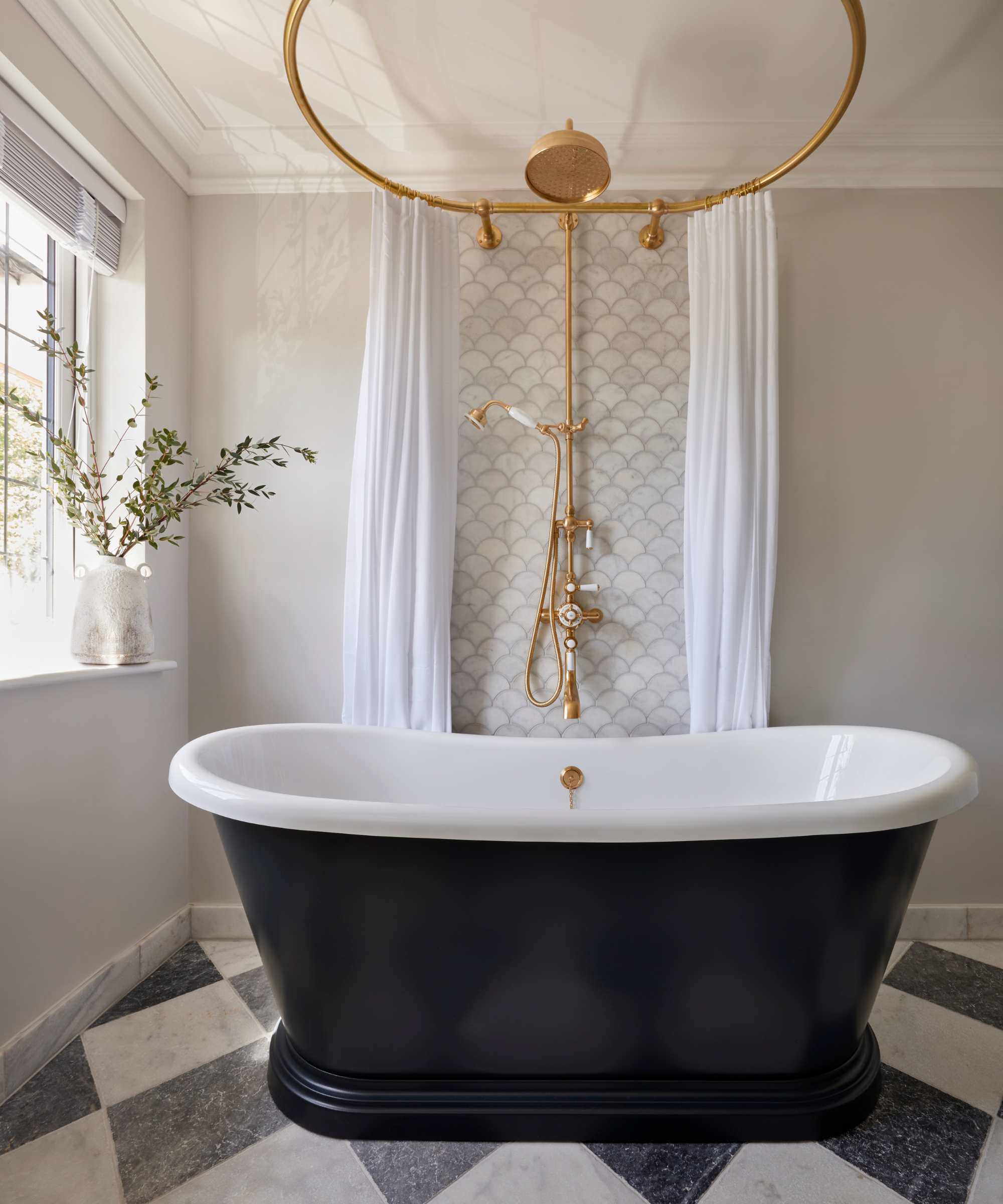 Elegant bathroom with a black freestanding tub, white interior, scalloped tile backdrop, brass shower ring, and soft neutral walls for a classic, luxurious feel.