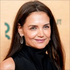 Katie Holmes in front of a plain backdrop on a red carpet