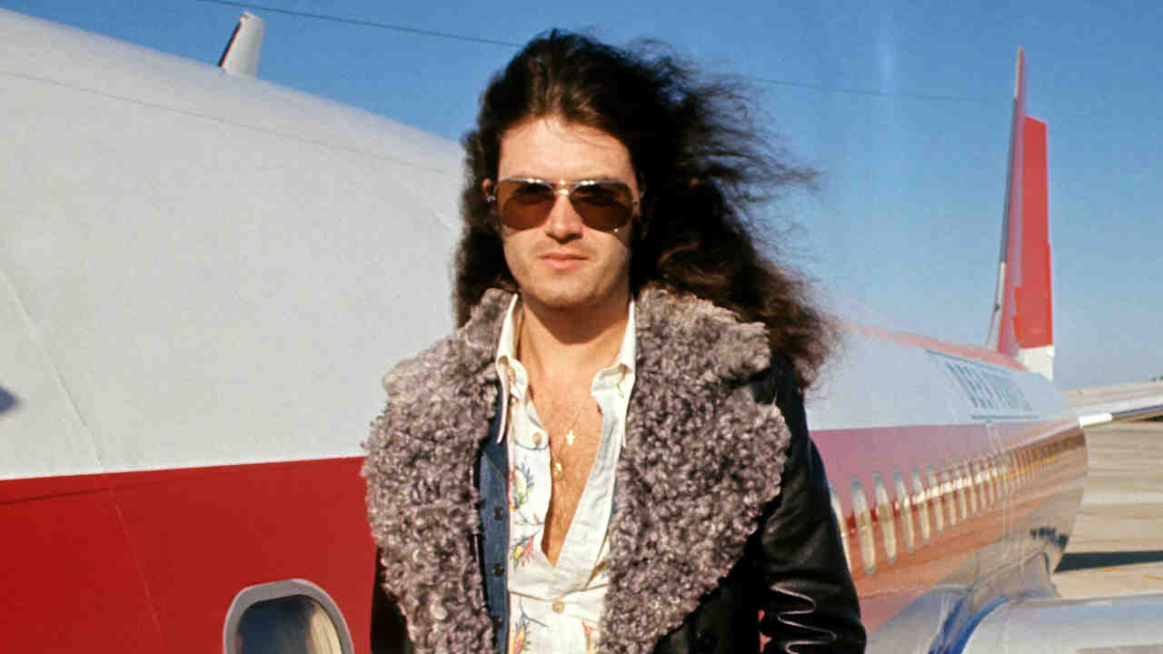 Glenn Hughes standing next to a jet plane in the 1970s
