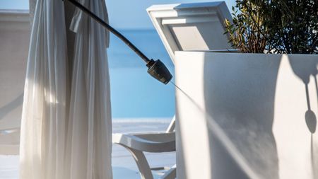 High-pressure jet washer in action cleaning a luxurious balcony setup with white curtains, chairs, and a potted plant on a clear sunny day.