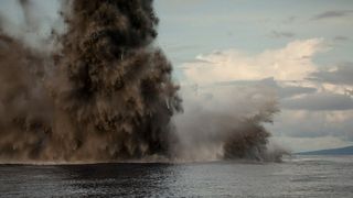 A giant plume of black smoke and water erupting from the sea's surface