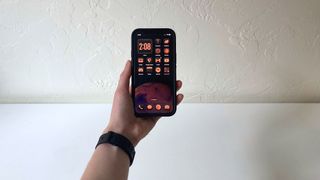 A person&#039;s hand holding an iPhone showing the home screen in iOS 18