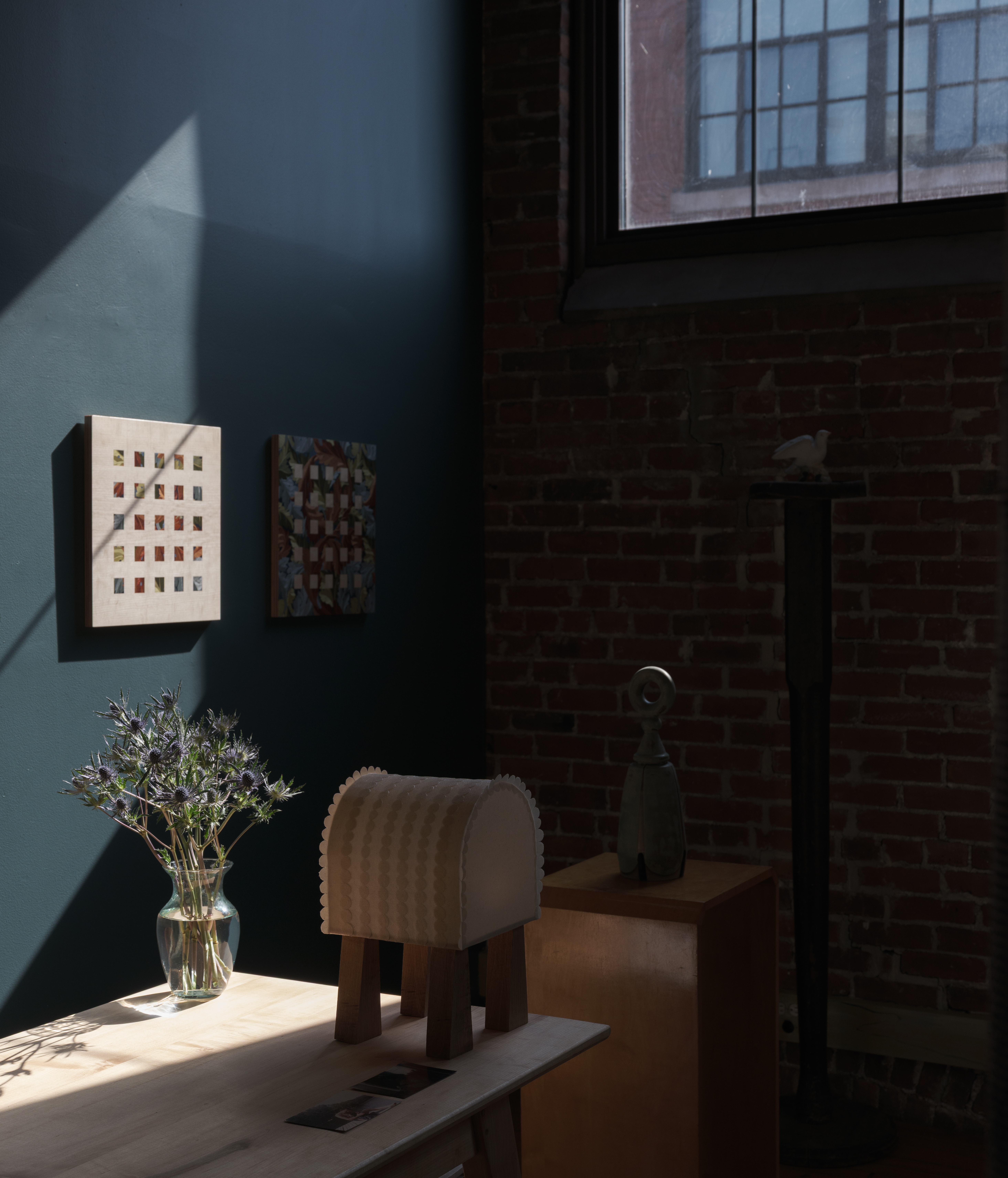 A gallery interior with a red-brick wall, and wood, ceramic, and bronze collectibles stacked atop wooden podiums.