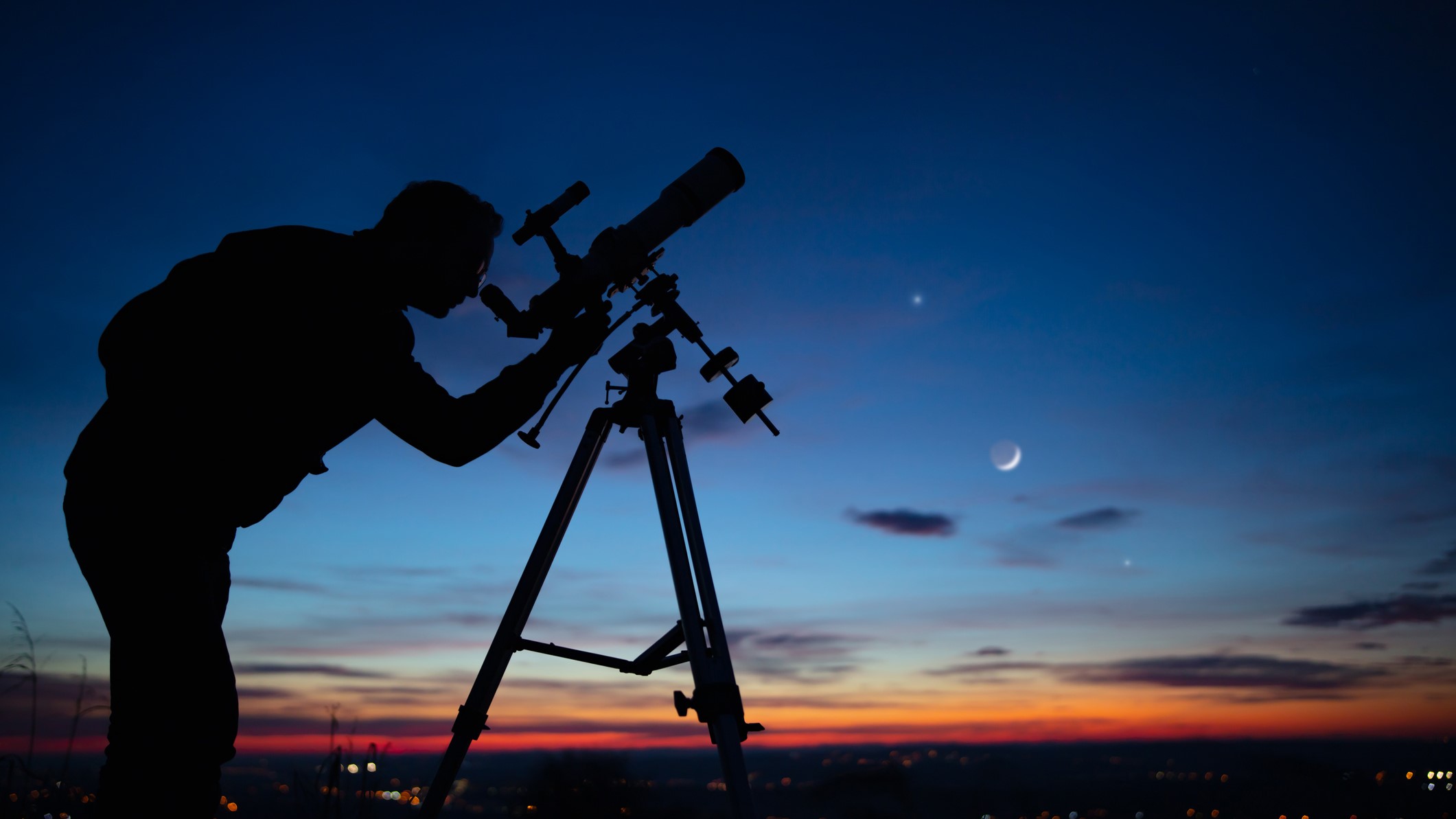 Silhouette of a man with a telescope looking at the sky.