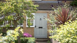 Brick house with white front door plus antique style letterbox and knocker surrounded by flowering plants and trees