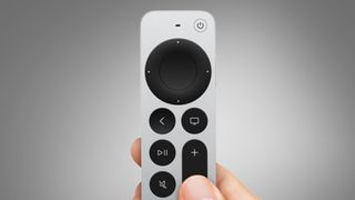 A hand holding the Apple TV remote on a grey background