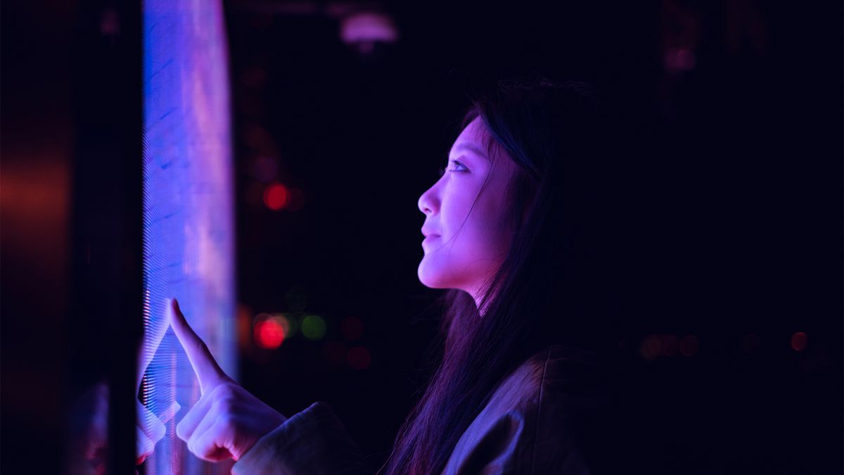 Female digital transformation specialist working on a touchscreen terminal in a darkened room with face illuminated by screen.