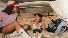 Two women wearing apparel from The North Face along with a bag from The North Face, while in the back of a van in the desert.