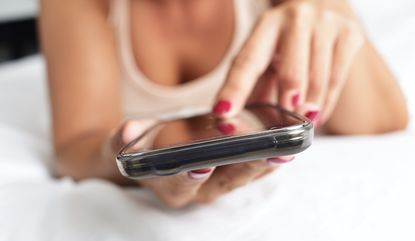 closeup of a young caucasian woman face down in bed using a smartphone, sext, sexting