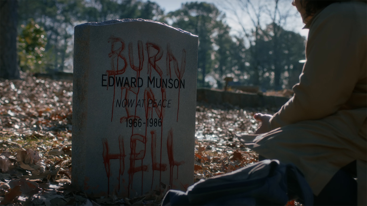 A screenshot of Eddie Munson's defaced gravestone that Dustin is kneeling by in Stranger Things season 5