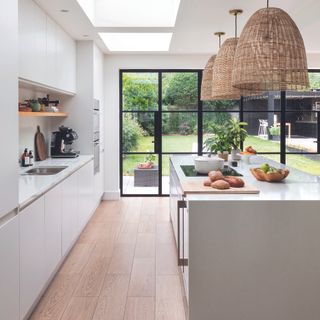 White modern kitchen with rattan lampshades over island