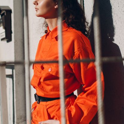 Woman in orange jumpsuit behind bars