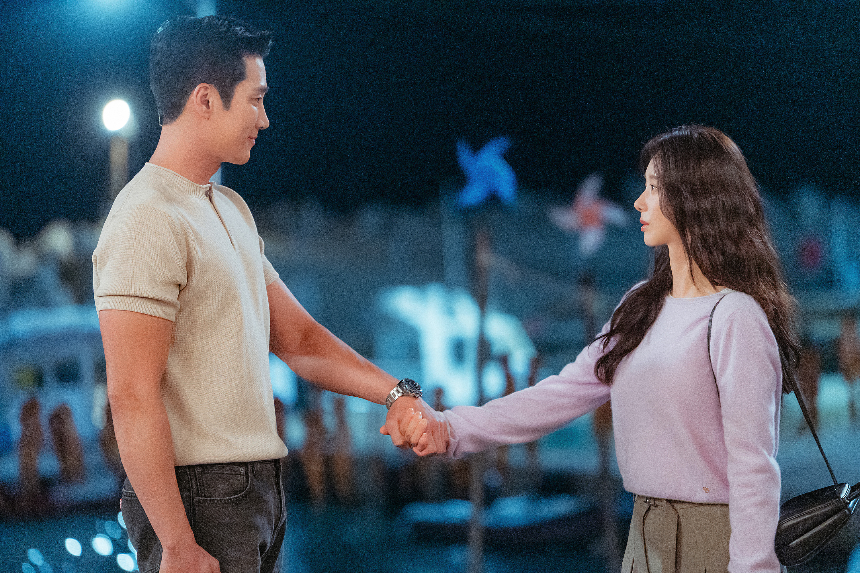 A man (actor Ahn Bo-hyun) and a woman (actress Lee Joo-bin) face each other and hold hands while standing outdoors at night. A still from the Prime Video K-drama 'Spring Fever.'