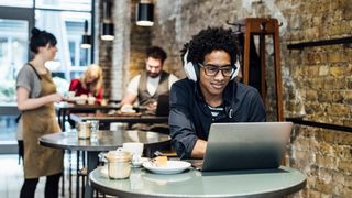 Shoulder surfing concept image showing a man working remotely in a coffee shop with laptop screen exposed and in sight of other customers.