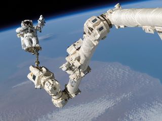 spacesuited astronaut on end of canadarm2. in the background is earth