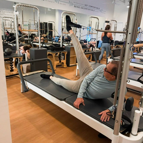 Man lying on his side using a Pilates reformer, one foot is in a stirrup and raised