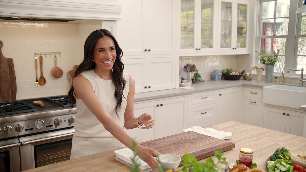 Meghan Markle in white kitchen with chrome range oven behind her