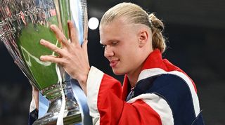 Erling Haaland, draped in the Norwegian flag, celebrates with the Champions League trophy after Manchester City's treble triumph in June 2023.