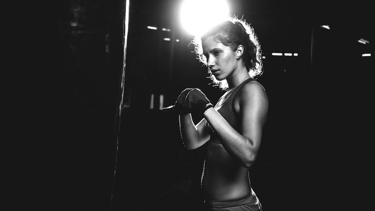black and white photo of a women in front of a punch bag in a gym 