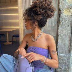 Influencer wears a lilac top and lilac bag.