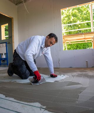 A man in a newly plasterboarded room screeding a floor featuring JK Floorheating bespoke channelled underfloor heating channels and pipes