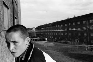 an industrial backdrop with a young person in the foreground, black and white