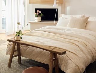 Off-white and cream bedding in a cozy bedroom. There is a wooden bench at the end of the bed