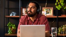 A man wearing headphones sits in front of a laptop at home