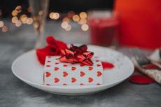 A small present wrapped in white and red heart patterned wrapping paper, with a red bow on top.