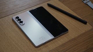 Två stycken Samsung Galaxy Z Fold 3 ligger nedåtvända på ett träfärgat bord bredvid en stylus.