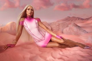 Paris Hilton laying in a pink sandy desert wearing a pink and white latex dress.