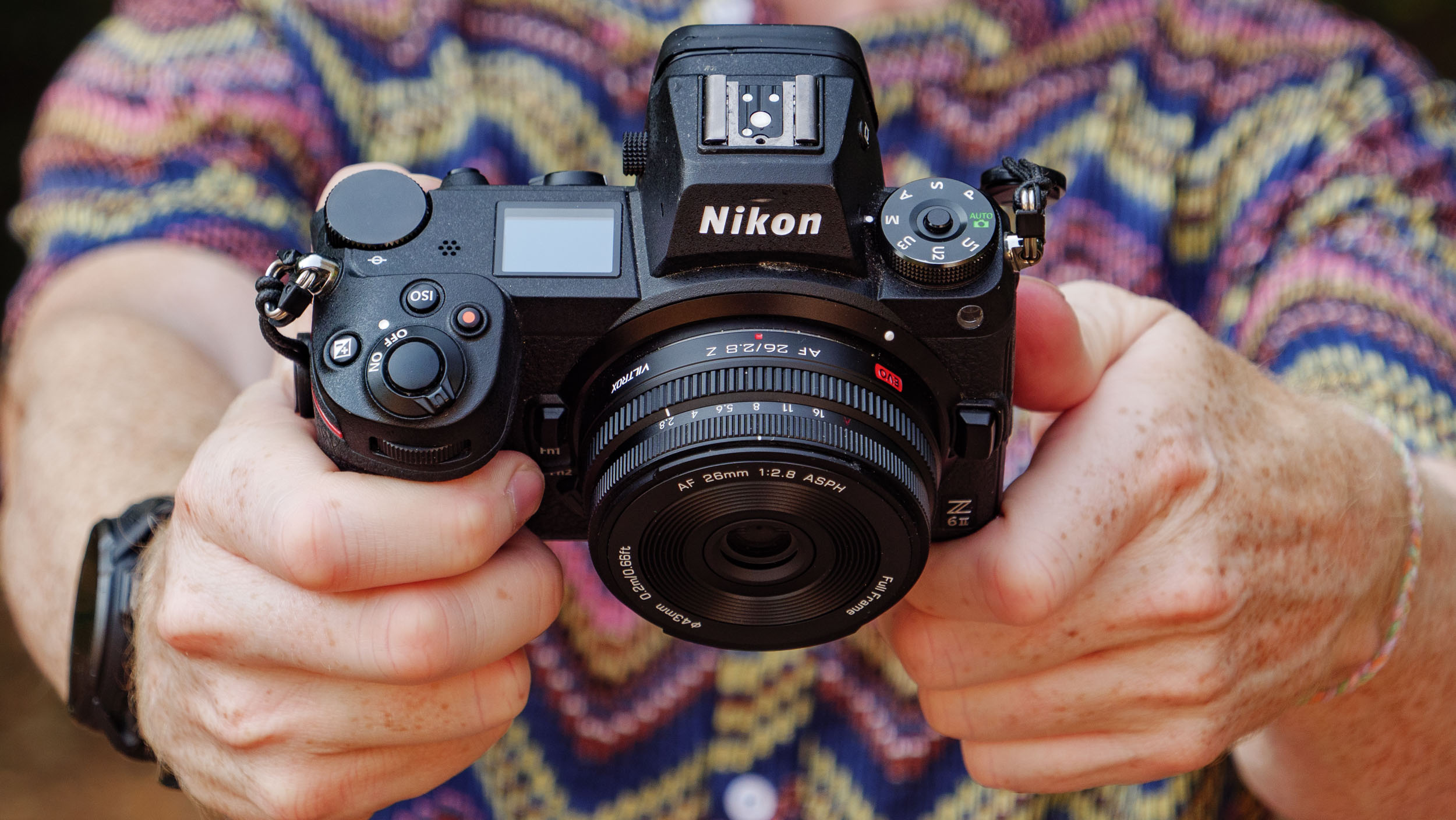 Viltrox AF 26mm F2.8 EVO 'pancake' lens attached to a Nikon mirrorless camera, photographer and TechRadar's Cameras Editor, Tim Coleman is holding the camera and is wearing a funky shirt