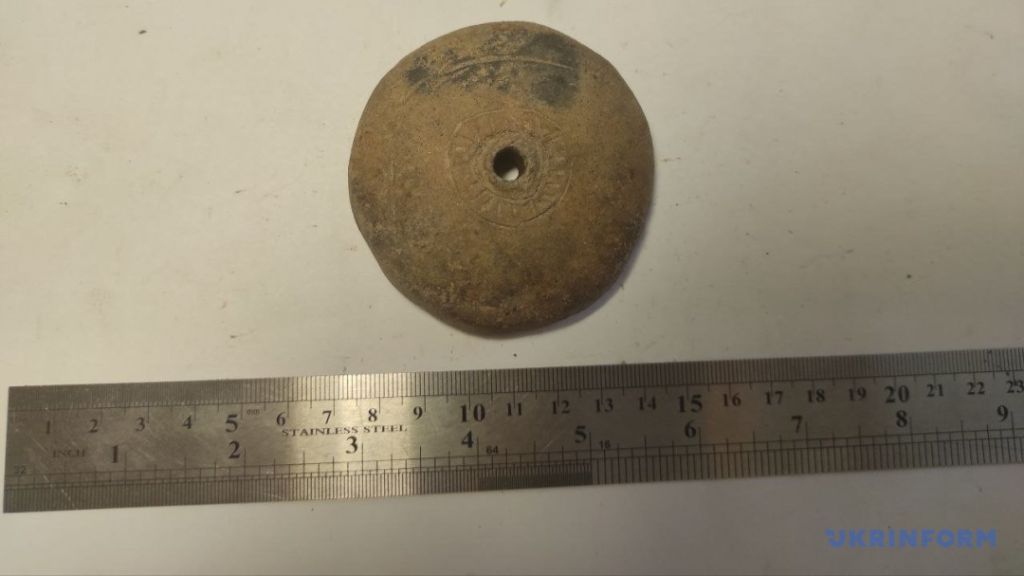 a flat circular artifact with a hole through the center; likely a spindle whorl used to weight spindles when hand-spinning yarn